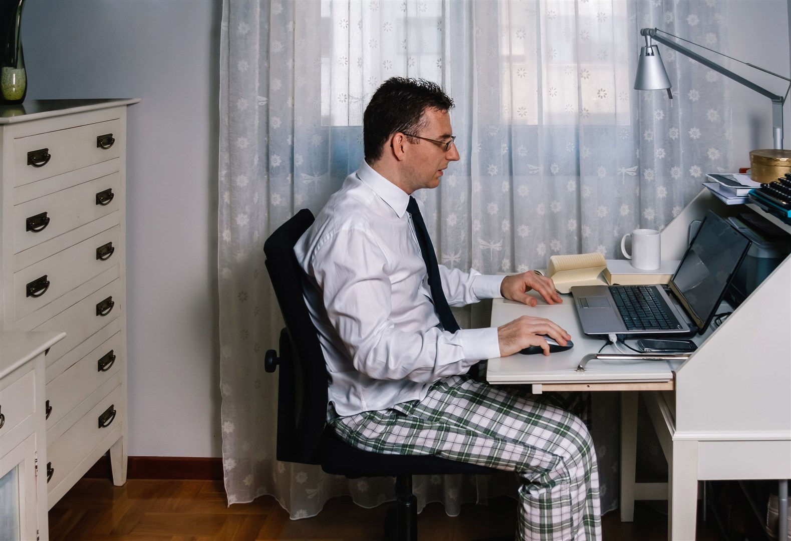 Man working from home with laptop wearing shirt, tie and pajama pants