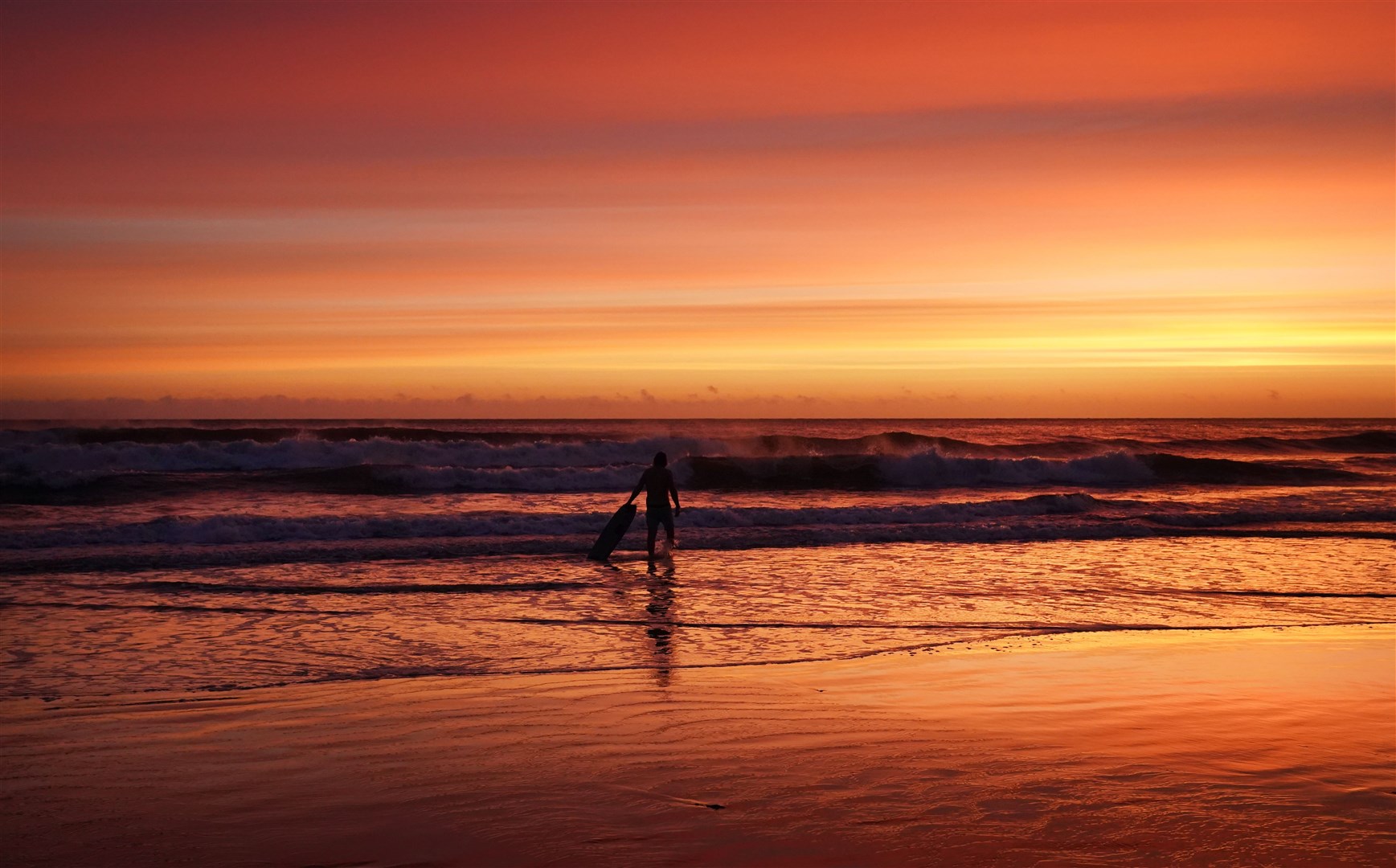 It was a freezing cold morning, but the orange sky and perfect waves were enough to tempt this surfer into the water at Tynemouth Longsands beach (Owen Humphreys/PA)