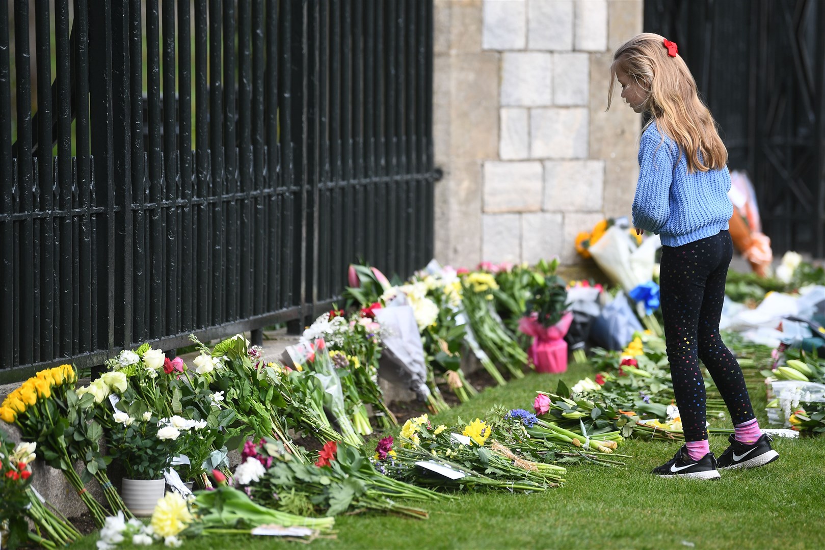 A young girl looks at flowers at Cambridge Gate at Windsor Castle, Berkshire, following the announcement of the death of the Duke of Edinburgh (Victoria Jones/PA)