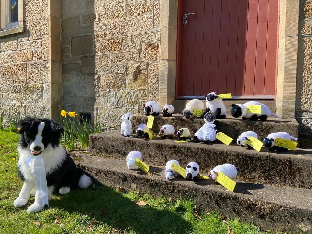 Knitted lambs and sheepdog pose on Parish Church steps.
