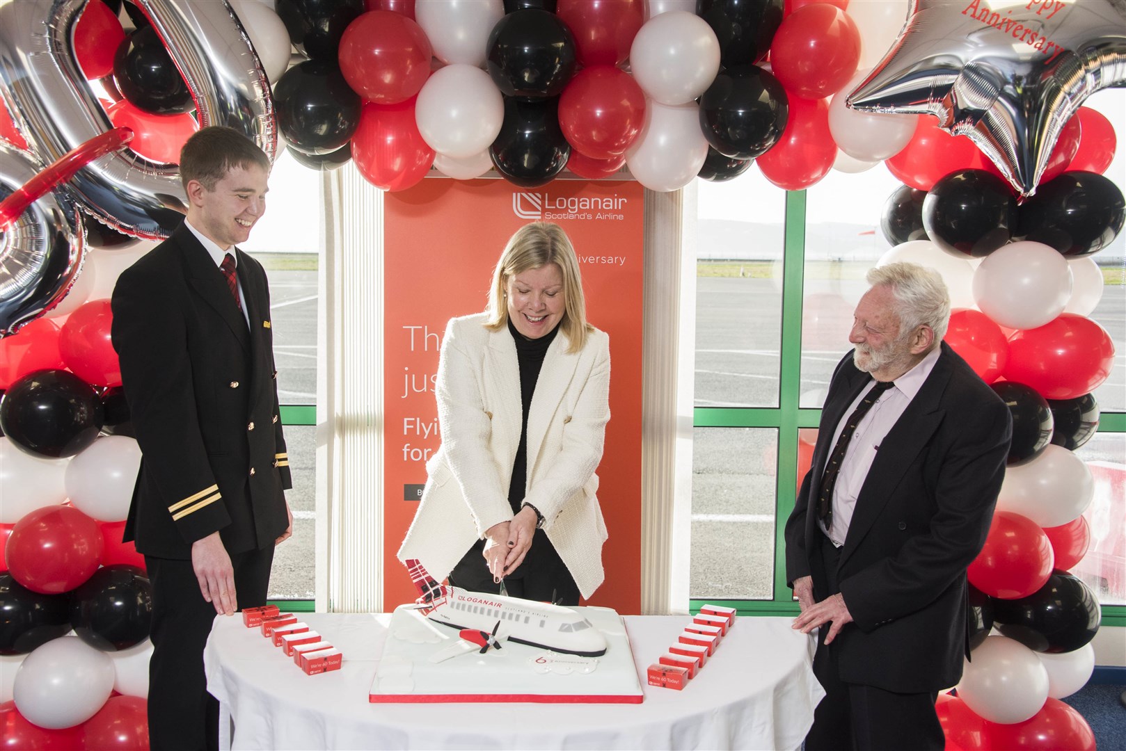 Loganair's chief commercial officer Kay Ryan is joined by serving pilot Aaron Dickson and 1970s skipper, Captain Geoff Rosenbloom, as she cuts into the specially designed Loganair anniversary cake. Photograph: Alan Richardson