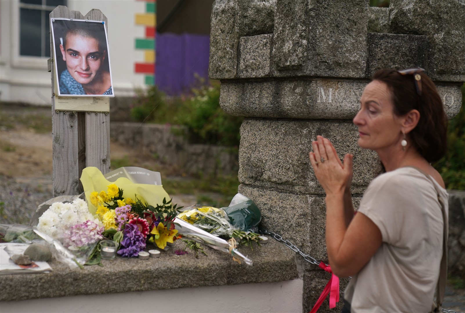 Olivia Galvin from Kerry holds her hands together in front of floral tributes laid outside Sinead O’Connor’s former home in Bray (Brian Lawless/PA)