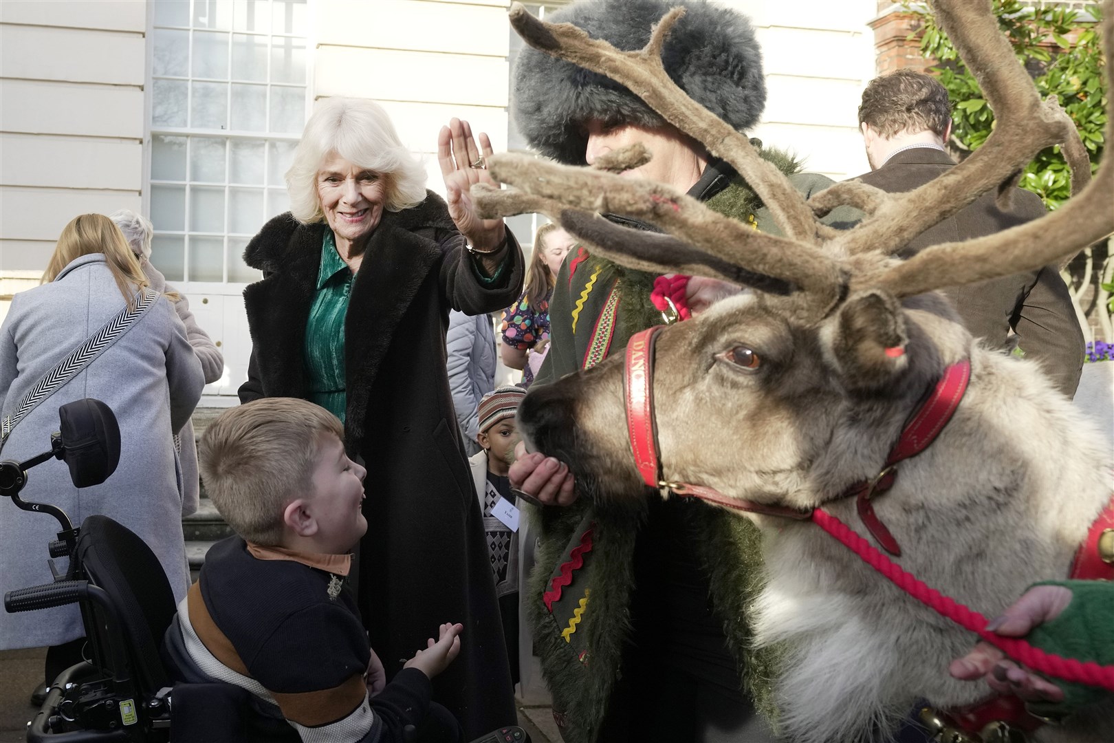 Camilla strokes a reindeer as one of her young guests watches (Kin Cheung/PA)