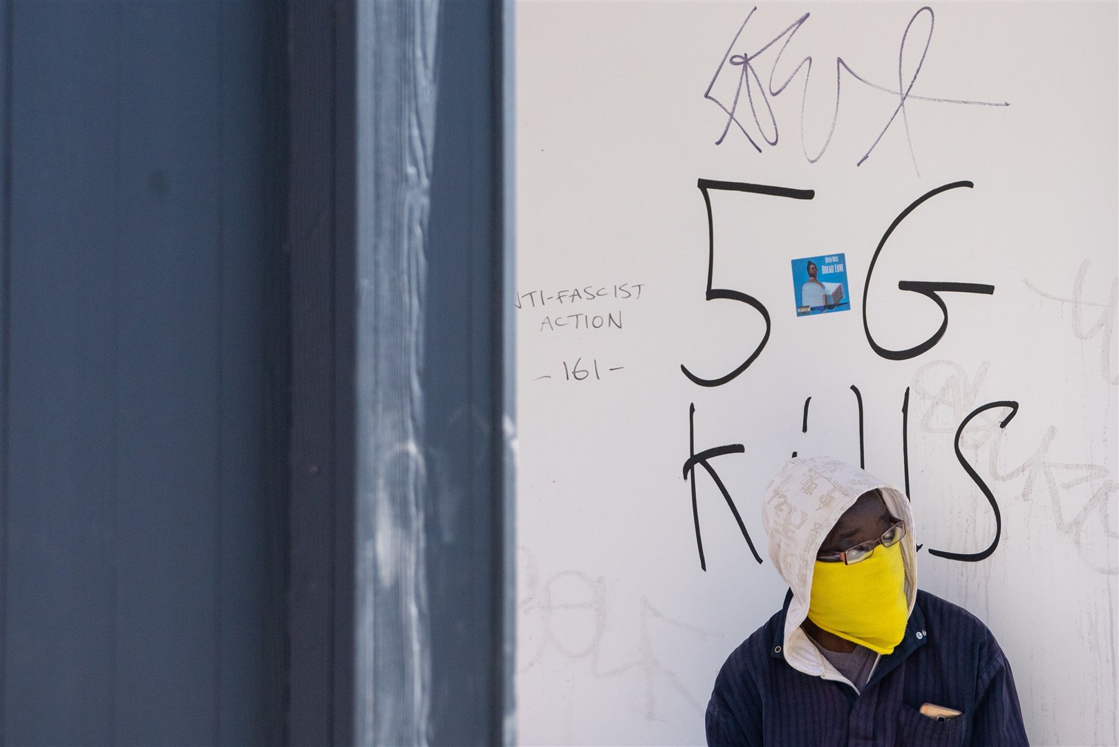 A person wearing a protective face mask sits alongside graffiti reading 5G Kills, in Shoreditch, east London (Dominic Lipinski/PA)