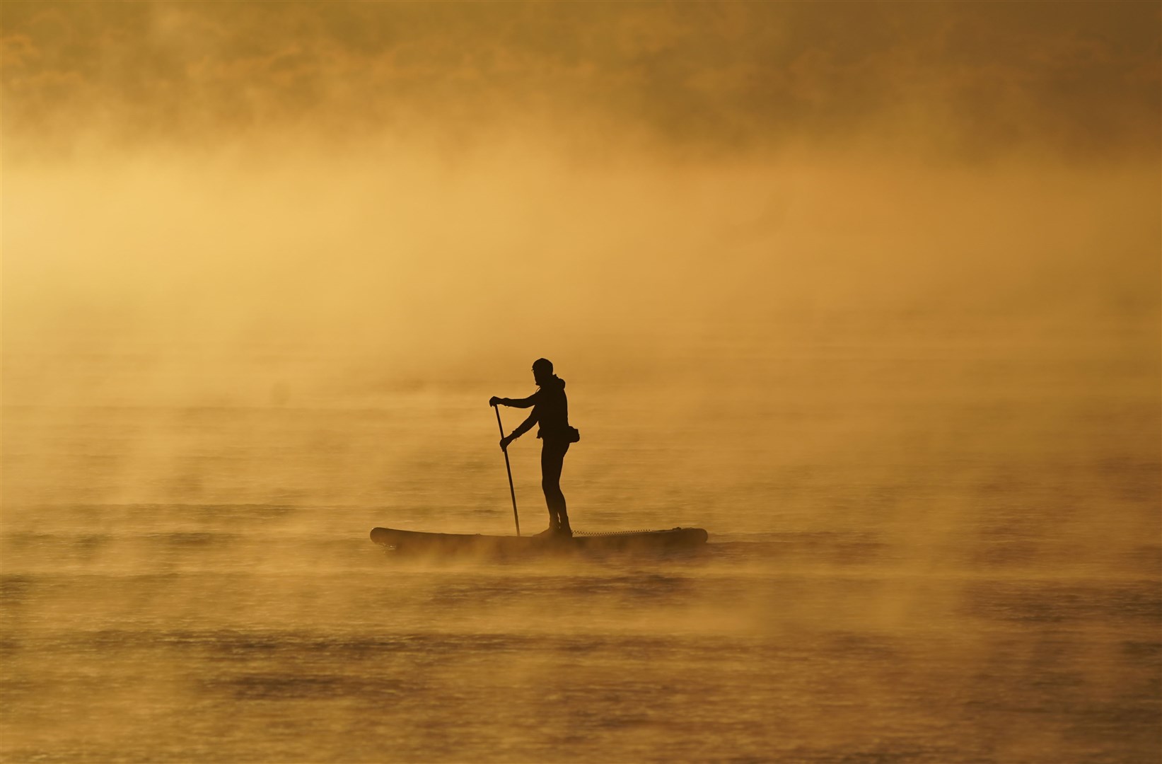 A paddle boarder makes his way through the sea mist off the coast of Avon Beach in Dorset (Andrew Matthews/PA)