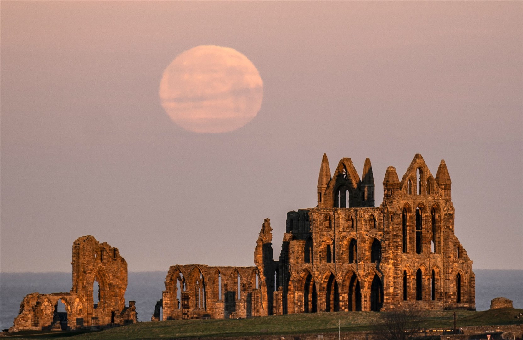 The moon looks closer than ever as it sets off the coast behind Whitby Abbey in North Yorkshire (Danny Lawson/PA)