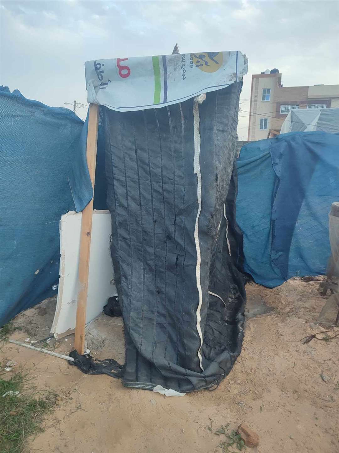 A hole in the ground shielded by tarpaulin serves as a toilet.