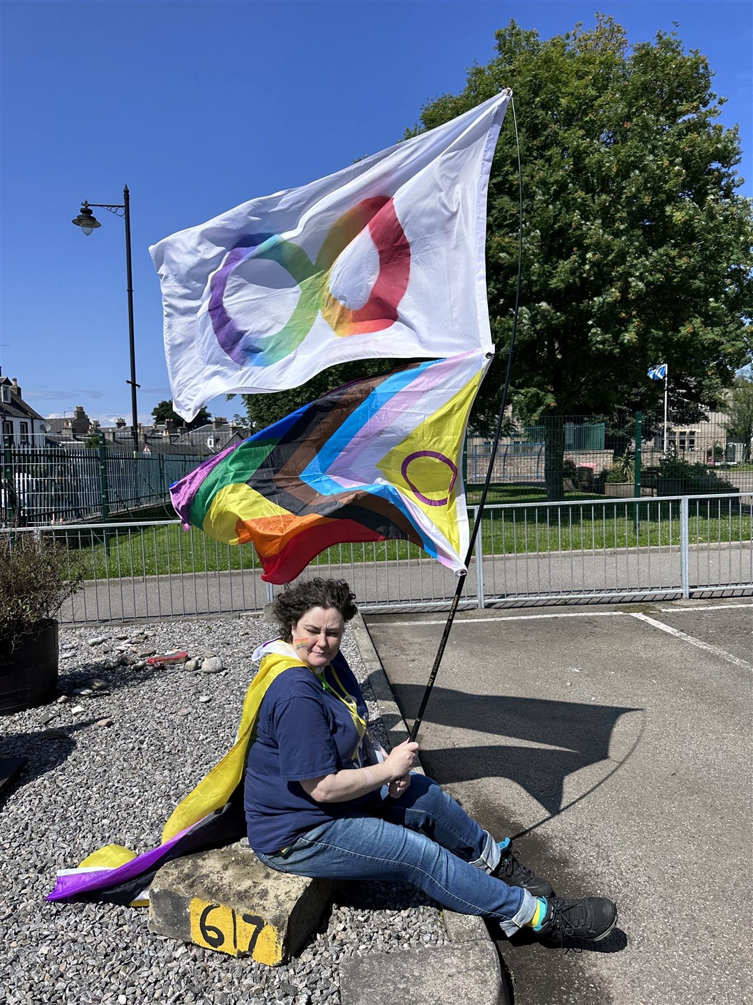 Kabie from the Autism Rights Group Highland committee proudly flying multiple flags at Highland Pride 2023.