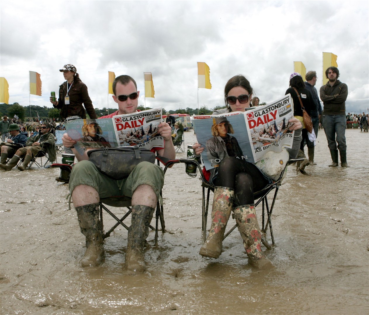A couple read the free paper at a previous wet Glastonbury Festival at Worthy Farm in Pilton, Somerset (Anthony Devlin/PA)