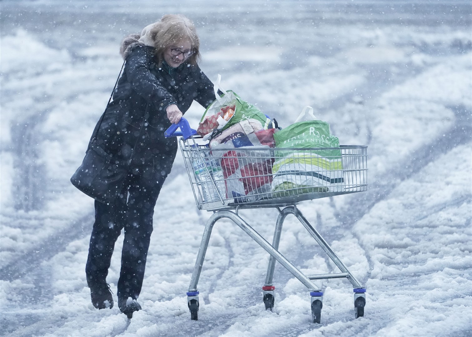 A woman pushes a shopping trolley through snow in Hexham (Owen Humphreys/PA)